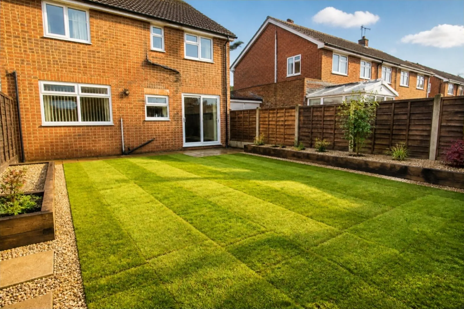 New striped back lawn with straight edges, a gravel strip and sleeper beds behind a brick house